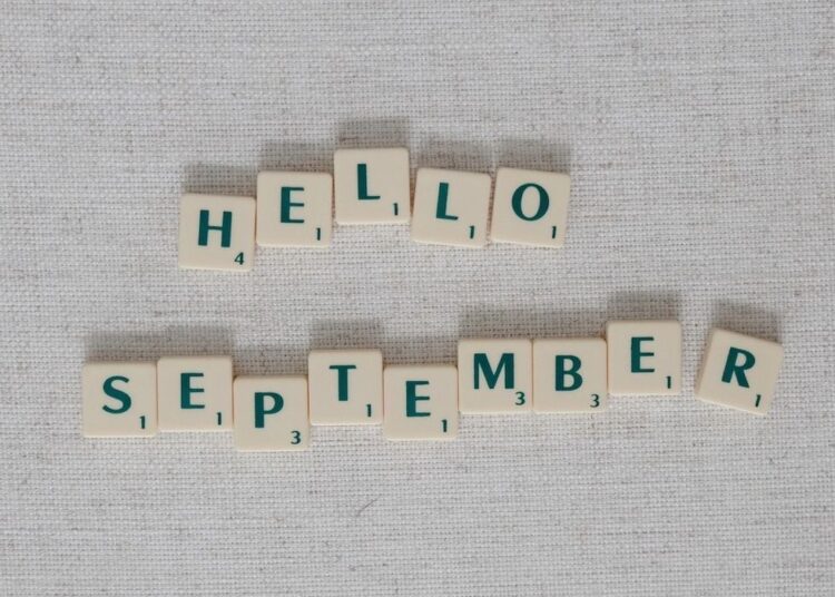 "Scrabble tiles spell 'Hello September' on a textured gray background."