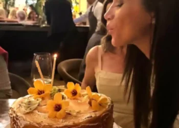 Woman blowing out a candle on a cake decorated with yellow flowers in an upscale restaurant