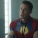 John Cena with a visitor badge on sitting at a prison table in Peacemaker Season 2.
