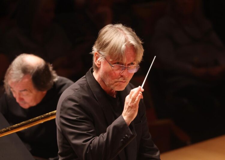 Man with white hair and glasses holding a conductor's wand