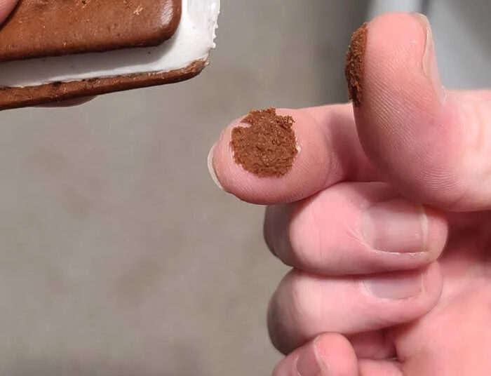 A partially eaten ice cream sandwich with some crumbs on a person's fingertip