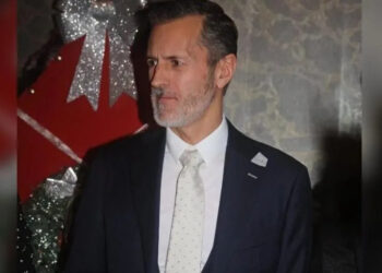 Tommy Traylen, who has greying hair, is wearing a black suit, white shirt and a white tie with pale blue spots.