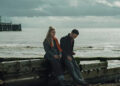 Imogen Poots as Laura and Brett Goldstein as Simon sitting by a pier and laughing in All of You