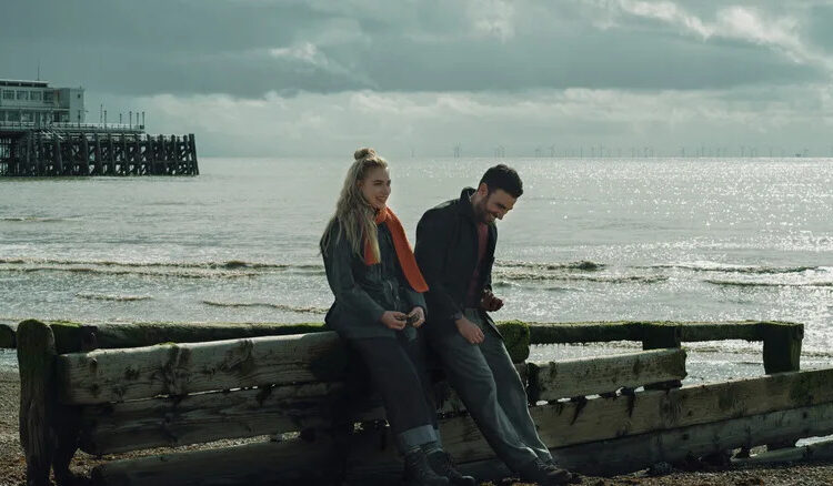Imogen Poots as Laura and Brett Goldstein as Simon sitting by a pier and laughing in All of You