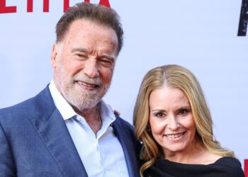 Arnold Schwarzenegger smiling on the red carpet with girlfriend Heather Milligan, both dressed elegantly