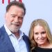 Arnold Schwarzenegger smiling on the red carpet with girlfriend Heather Milligan, both dressed elegantly