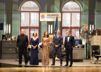 Five people on a stage with a recreation of a set of a New York police office.