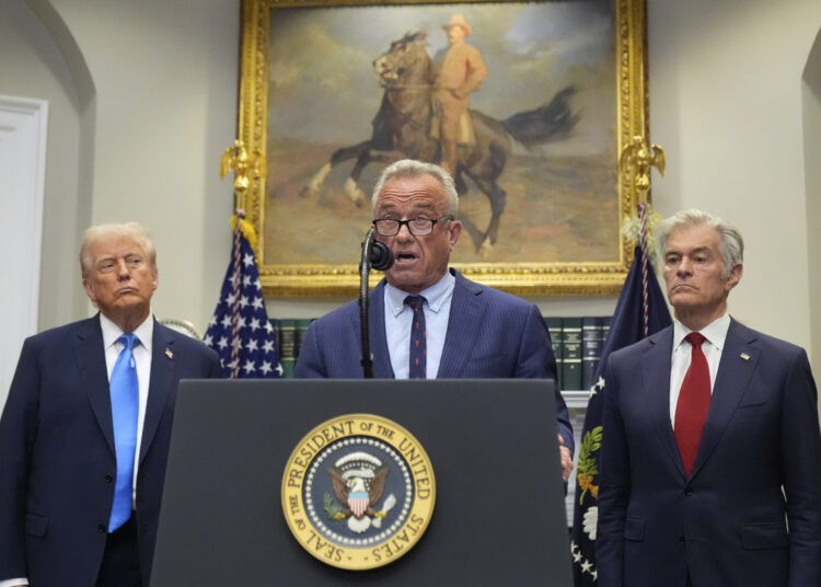 Three men stand at a podium with the Seal of the President of the United States, flanked by flags and a painting of a rider on horseback in the background.