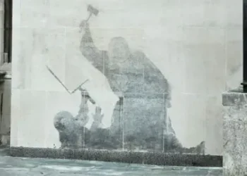 PA Media Banksy mural of a judge attacking a protestor with a gavel. The painting has been washed away, so the details are not visible, leaving a grey shadowy silhouette.