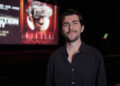 Film director, Derry Shillitto, stood in the auditorium of Broadway Cinema, Nottingham, with a projection of The Correction Unit film poster in the background.