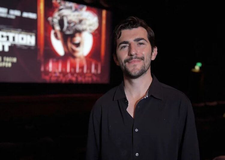 Film director, Derry Shillitto, stood in the auditorium of Broadway Cinema, Nottingham, with a projection of The Correction Unit film poster in the background.
