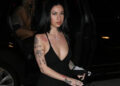 Bhad Bhabie exits a car wearing a form-fitting black dress with a deep V-neck, showcasing her tattoos