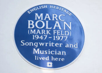 A close up of a blue English Heritage plaque on a white wall.