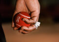 A hand holding a red tennis ball with