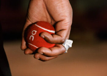 A hand holding a red tennis ball with