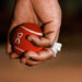 A hand holding a red tennis ball with