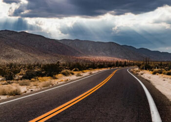 Desert highway in Southern California on a cloudy day with sunbeams breaking through.