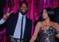 Offset and Cardi B pose together. Offset wears a suit and flashes a peace sign, while Cardi B is in a metallic dress, set against pink tinsel.