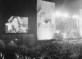 John Cougar Mellencamp performs both on stage and on one of two large screen television screens set up at the University of Illinois Memorial Stadium in Champaign, Ill. on Sept. 22, 1985 during the Farm Aid concert. (AP Photo/Seth Perlman, file)