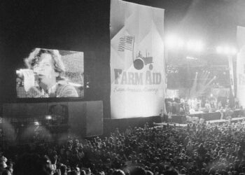 John Cougar Mellencamp performs both on stage and on one of two large screen television screens set up at the University of Illinois Memorial Stadium in Champaign, Ill. on Sept. 22, 1985 during the Farm Aid concert. (AP Photo/Seth Perlman, file)