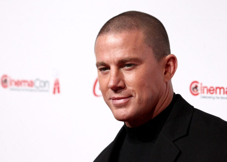 Channing Tatum poses on the red carpet in a black suit and turtleneck at CinemaCon, wearing a close-cropped haircut.