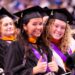 Two smiling graduates in caps and gowns giving thumbs up at a graduation ceremony.