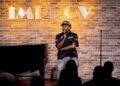 Man sitting on a stool performing at the Improv