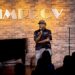 Man sitting on a stool performing at the Improv
