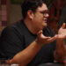 Comedian Caleb Hearon gesturing at a table with his hands, elbows on the table. Caption reads, "I legitimately thought it was funny."