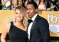 Mariah Carey and Nick Cannon pose together on a red carpet. Mariah wears a black dress, and Nick is in a tuxedo.