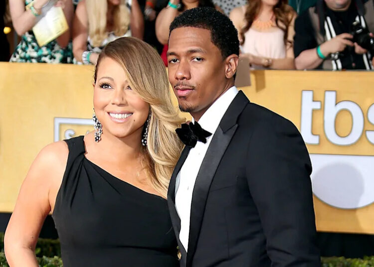 Mariah Carey and Nick Cannon pose together on a red carpet. Mariah wears a black dress, and Nick is in a tuxedo.