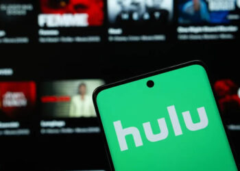 smartphone with hulu logo in front of a tv showing streaming library
