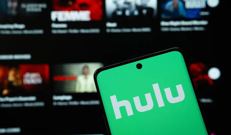 smartphone with hulu logo in front of a tv showing streaming library