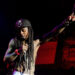 Lil Wayne performing on stage, shirtless, wearing a cap and holding a microphone with his right arm raised.