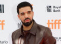 Drake at the Toronto International Film Festival, wearing a brown leather jacket, posing against a backdrop with TIFF logos.