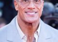 Dwayne Johnson smiling in a light gray suit at a red carpet event