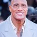 Dwayne Johnson smiling in a light gray suit at a red carpet event