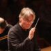 Man with white hair and glasses holding a conductor's wand