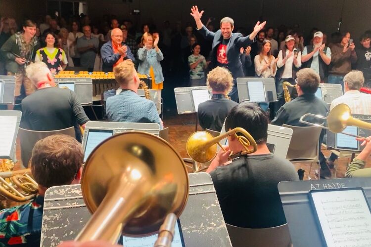 A lively band performance with musicians enthusiastically playing instruments while a cheering audience applauds in the background.