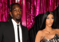 Offset in a black suit and Cardi B in a metallic dress stand in front of pink tinsel curtains, posing for a photo.