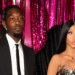 Offset in a black suit and Cardi B in a metallic dress stand in front of pink tinsel curtains, posing for a photo.