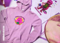 A purple hoodie and white t-shirt featuring Barney designs, notebooks, a CD, and a pen on a pastel background.
