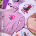 A purple hoodie and white t-shirt featuring Barney designs, notebooks, a CD, and a pen on a pastel background.