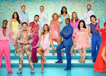 Fifteen men and women dressed in colourful ballroom dancing outfits standing on turquoise steps, with glitter falling around them. They are all posed in various  dancing postures.