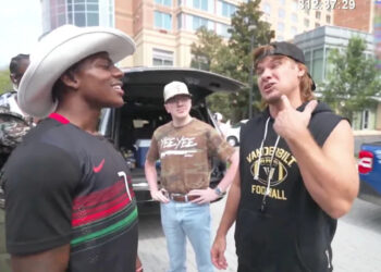 A group of people are standing outside near a vehicle. Streamer IShowSpeed wears a cowboy hat and comedian Theo Von has a sleeveless Vanderbilt Football shirt.