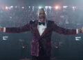 Colman Domingo's Bobby Thompson announcing The Running Man TV show with his arms outstretched.