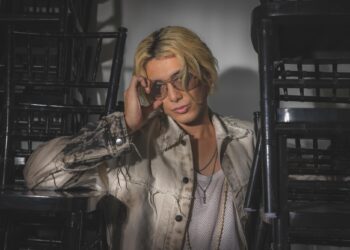 Man with bleach blond hair waring sun glasses posing with stacks of chairs