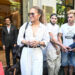 Jennifer Lopez, dressed in a striped blouse and white trousers, holds a coffee cup as she stands outside surrounded by fans and onlookers.