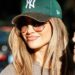 ennifer Lopez wears oversized sunglasses and a green New York Yankees cap while smiling outdoors.