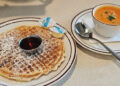 Waffle with powdered sugar on a white plate and soup in a white bowl at Waffle House